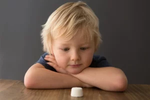 Child sitting at table staring at a marshmallow.