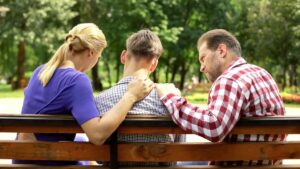 Parents sitting by their son with their hands on his shoulders.